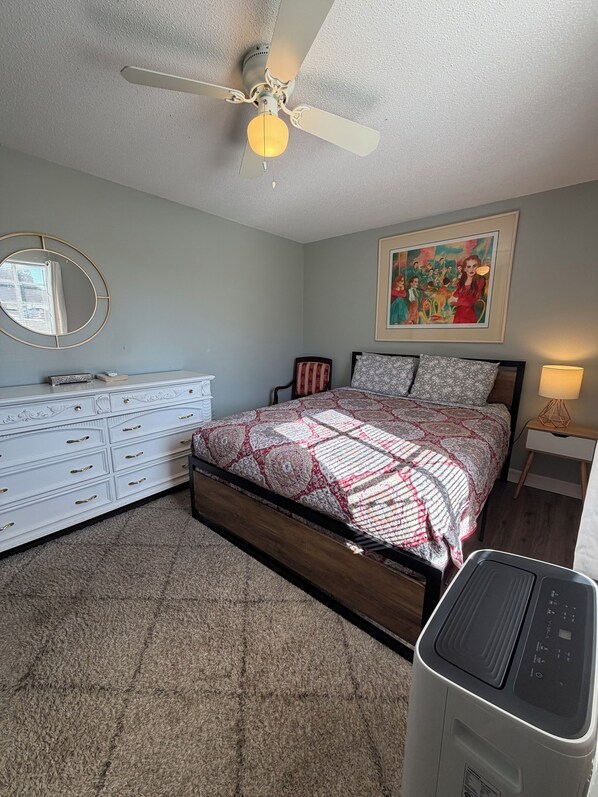 Une chambre à coucher avec un lit, une commode, un ventilateur de plafond et un tableau accroché au mur.