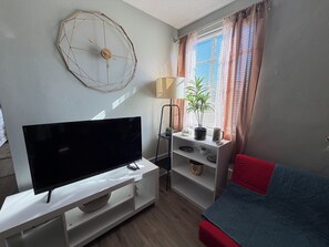Un salon moderne avec un téléviseur à écran plat, une horloge murale décorative, une plante en pot et un canapé rouge.