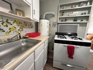 A compact kitchen with a sink, stove, and shelves with various kitchenware.