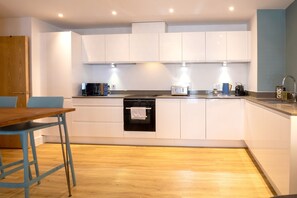 Une cuisine moderne avec des meubles blancs, une table en bois et un four noir.