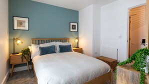 A bedroom with a wooden bed, two bedside tables with lamps, a radiator, and a door to another room.