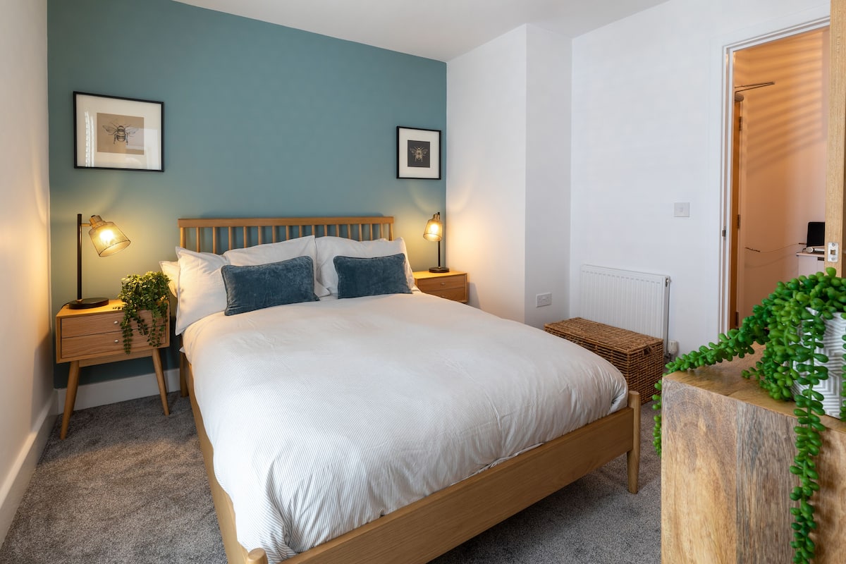 Un dormitorio con una cama de madera, dos mesitas de noche con lámparas, un radiador y una puerta a otra habitación.