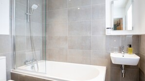 A modern bathroom with a glass-enclosed shower, a white bathtub, and a sink with a mirror above it.