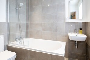 Une salle de bain moderne avec une douche à parois de verre, une baignoire blanche et un lavabo surmonté d’un miroir.