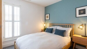 A bedroom with a bed, bedside tables, a window with blinds, and framed pictures on the wall.
