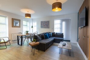 A modern living room with a sectional sofa, a dining table with chairs, a coffee table, and a television mounted on the wall. - Orchard Point (Southampton)