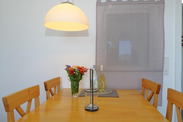 A dining table with four wooden chairs, a vase of flowers, a bottle of wine, and a glass.