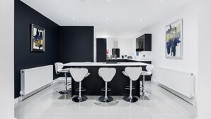 Une cuisine moderne avec un îlot central, des tabourets de bar blancs et un mur d’accent noir.