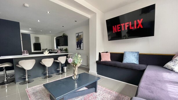 Un salon moderne avec un canapé noir, une table basse et un téléviseur fixé au mur qui affiche le logo « NETFLIX ».