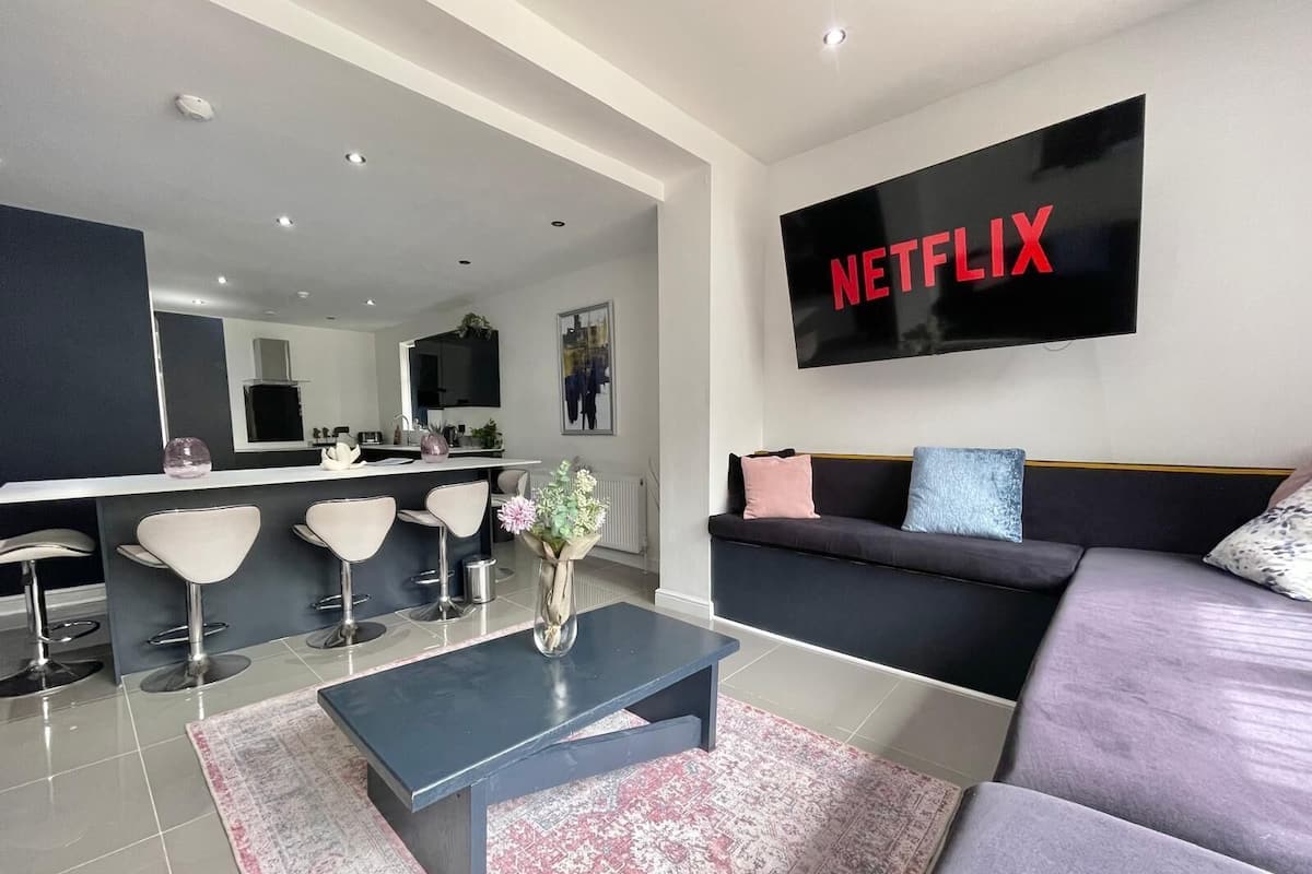 A modern living room with a black sofa, a coffee table, and a TV mounted on the wall displaying "NETFLIX".