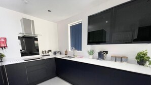 Une cuisine moderne avec des meubles noirs, un plan de travail blanc, une cuisinière encastrée et une grande fenêtre agrémentée de rideaux bleus.