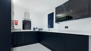 Une cuisine moderne avec des meubles de couleur sombre, des plans de travail blancs et une grande fenêtre.
