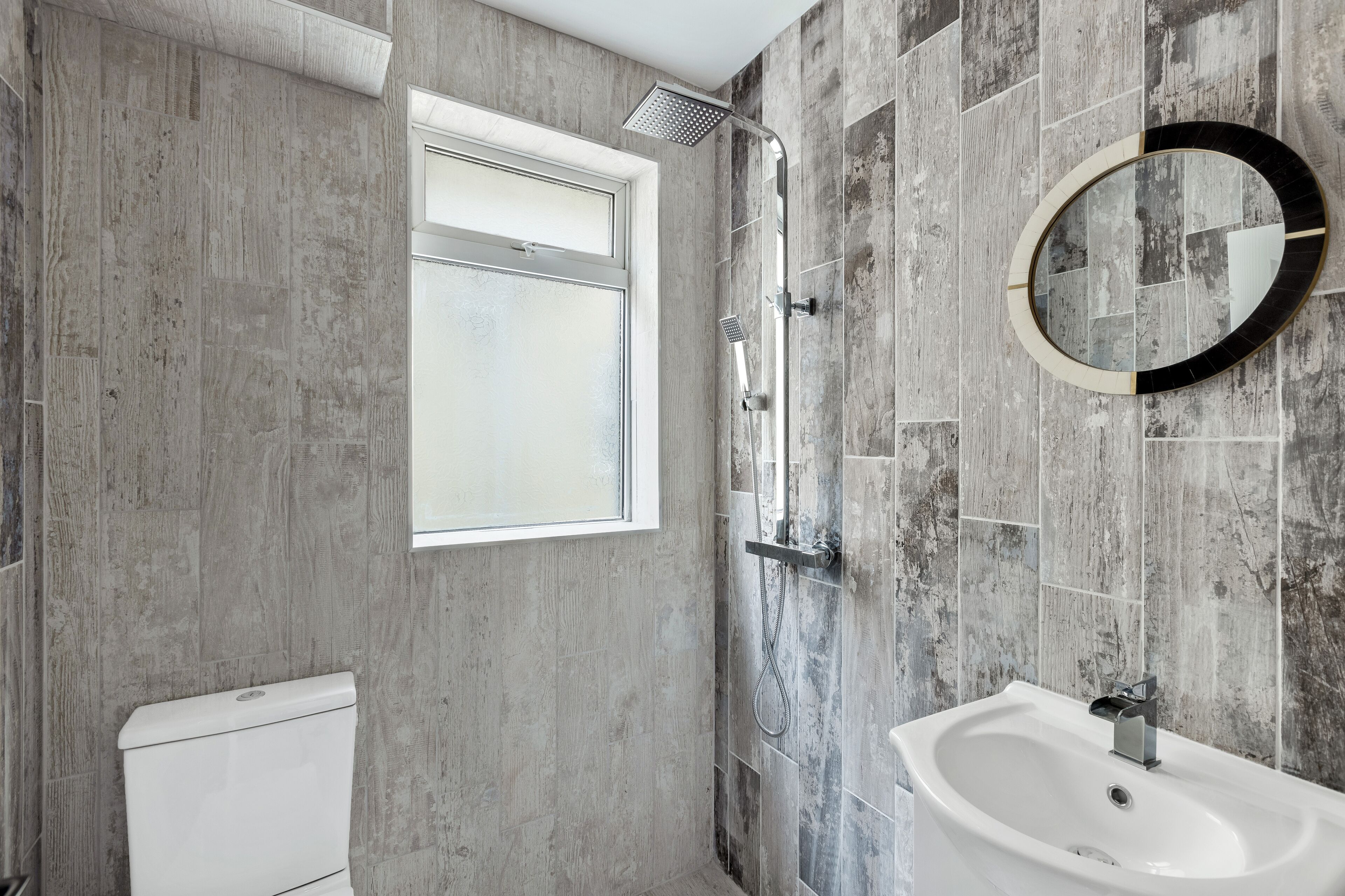 Ein Badezimmer mit Dusche, Toilette und Waschbecken, ausgestattet mit einem großen Spiegel und einem Fenster.