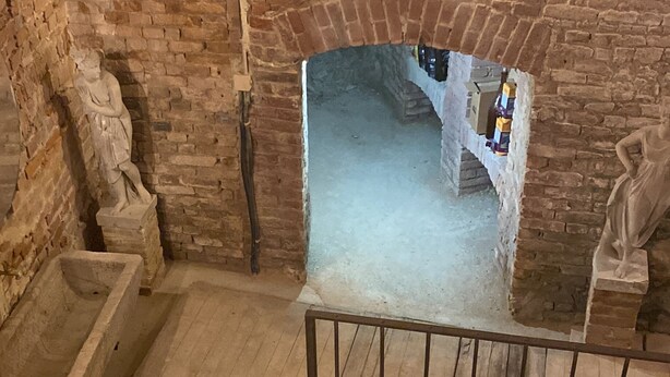 Una escalera que baja a un nivel inferior, con un muro de ladrillo y una estatua a la izquierda.