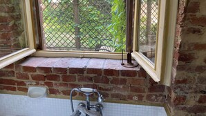 Un baño con ventana, pared de ladrillo y suelo de baldosas.