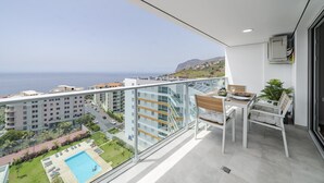 A balcony with a view of the sea, a pool, and a dining area with a table and chairs.