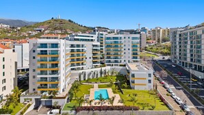 A modern hotel complex with multiple high-rise buildings, a central courtyard with a pool, and a view of a hilly landscape in the background.