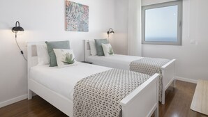 A bedroom with two beds, a large window, and a ceiling light fixture.