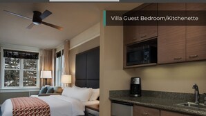 Habitación de hotel con cama, mesita de noche, lámpara y vista a árboles.