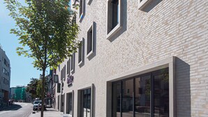 A modern building with a brick facade, large windows, and a tree in front. - RiKu HOTEL Göppingen (Goeppingen)