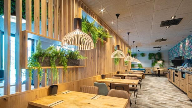 A modern restaurant interior with wooden paneling, hanging plants, and a herringbone floor pattern. - RiKu HOTEL Göppingen (Goeppingen)