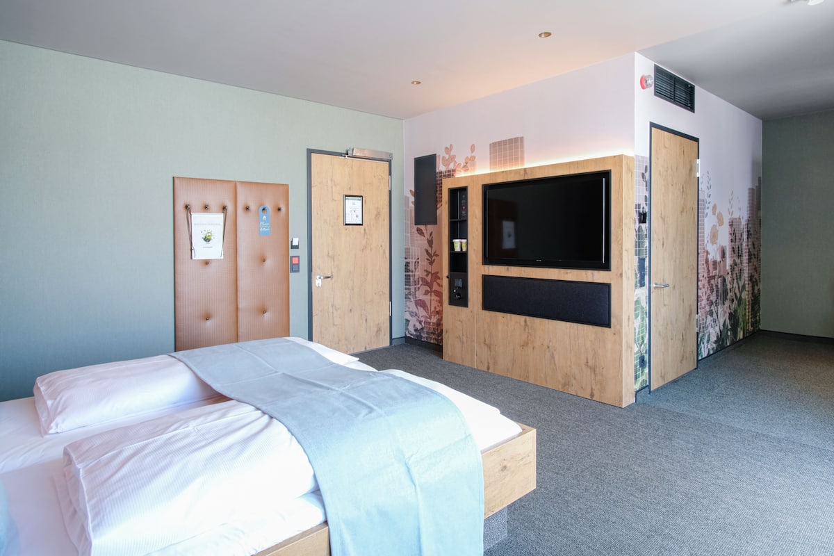 A hotel room with a bed, a wardrobe, a television, and a small desk area.