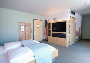 A hotel room with a bed, a wardrobe, a television, and a small desk area.
