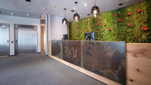 A reception area with a green wall, a wooden reception desk, and two elevators. - RiKu HOTEL Göppingen (Goeppingen)