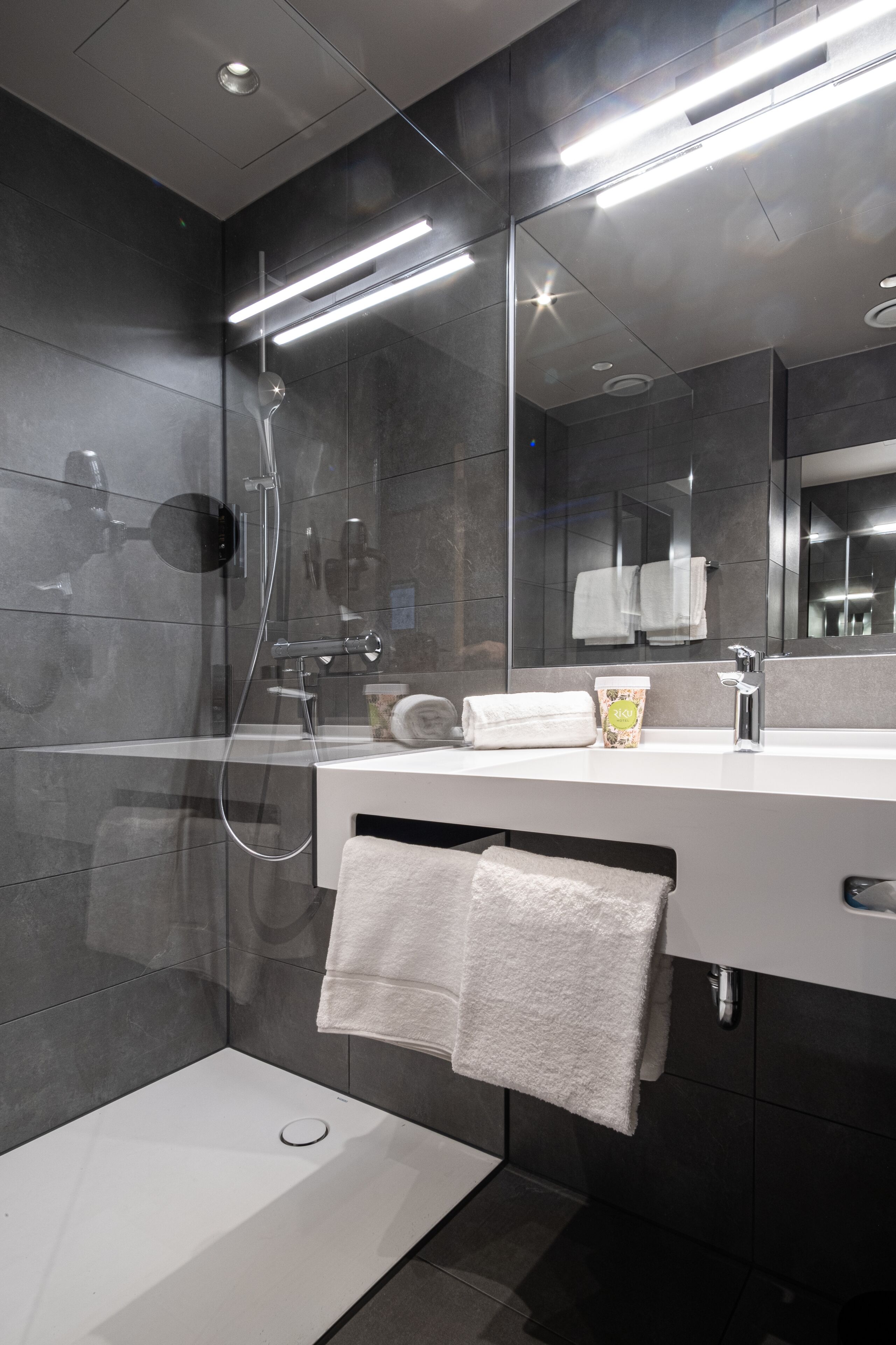 A modern bathroom with a glass-enclosed shower, a white sink, and a large mirror.