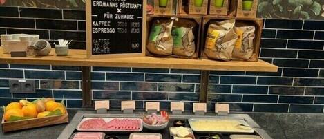 A breakfast buffet with various meats, cheeses, and fruits, along with a coffee station and a chalkboard menu.