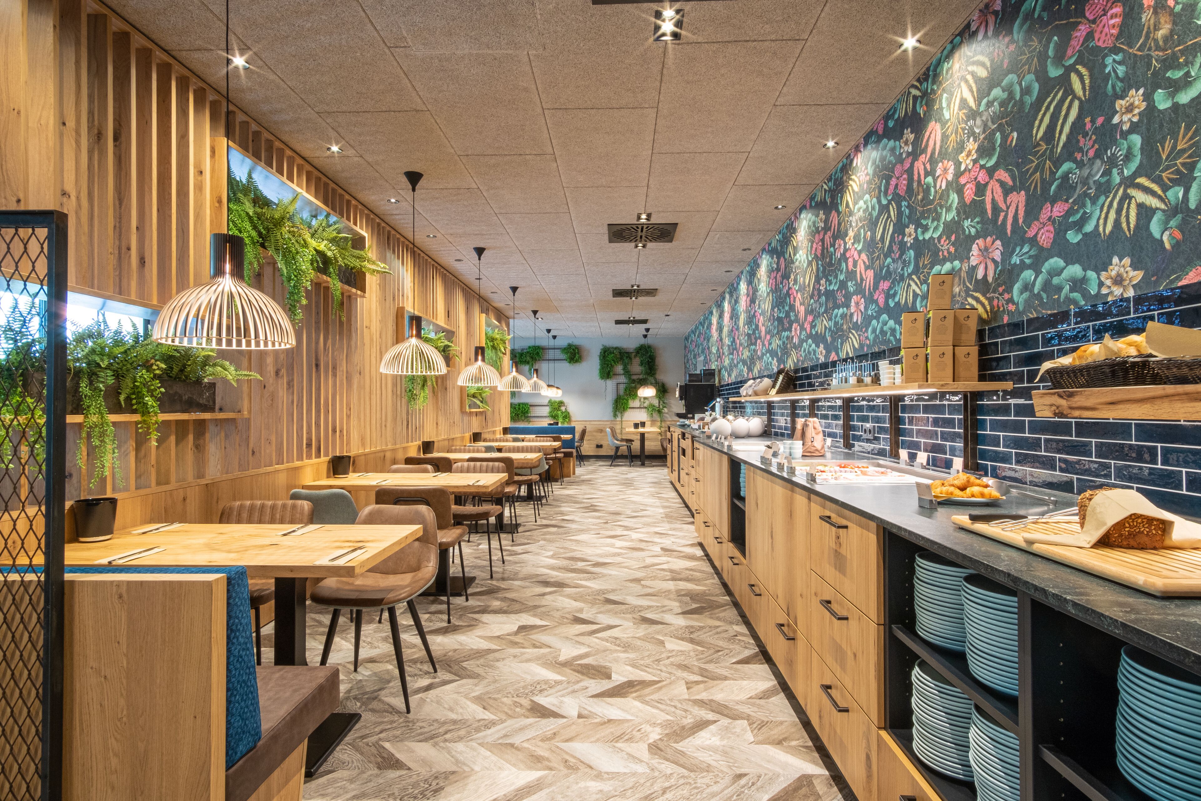 Un restaurante con paredes de paneles de madera, suelo con diseño de espiga, lámparas colgantes y una barra de cocina con platos azules.