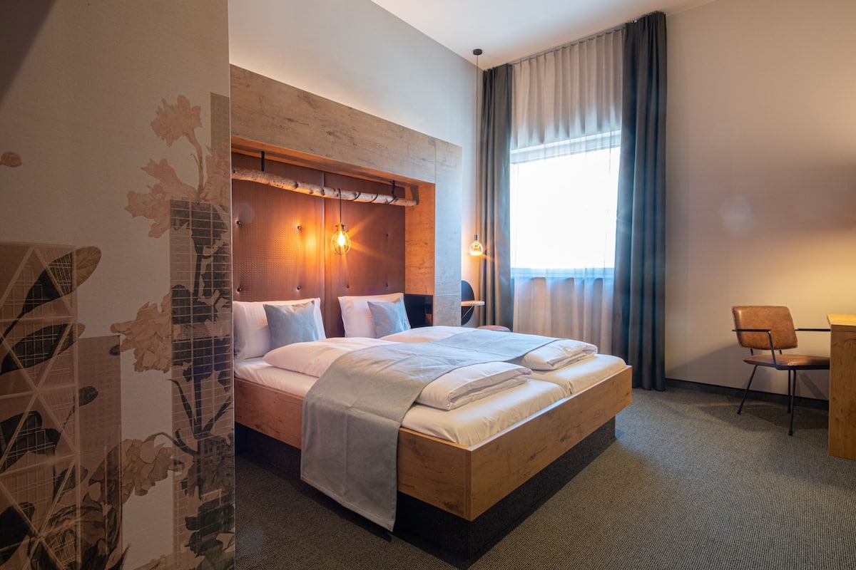 A hotel room with a wooden bed, a desk, a chair, and a large window with curtains.