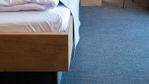 A modern hotel room with a wooden headboard, a large bed with white linens, a round wall-mounted light fixture, and a small stool. - RiKu HOTEL Göppingen (Goeppingen)