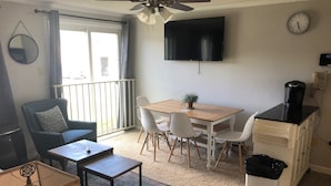 Un espacio habitable compacto con zona de comedor, un sofá, una cafetera, un televisor y un reloj en la pared.