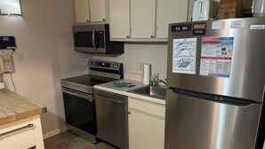 Cocina moderna con electrodomésticos de acero inoxidable, incluyendo un refrigerador, microondas, horno y lavavajillas. Hay un bote de basura y una encimera con dispensador de toallas de papel.