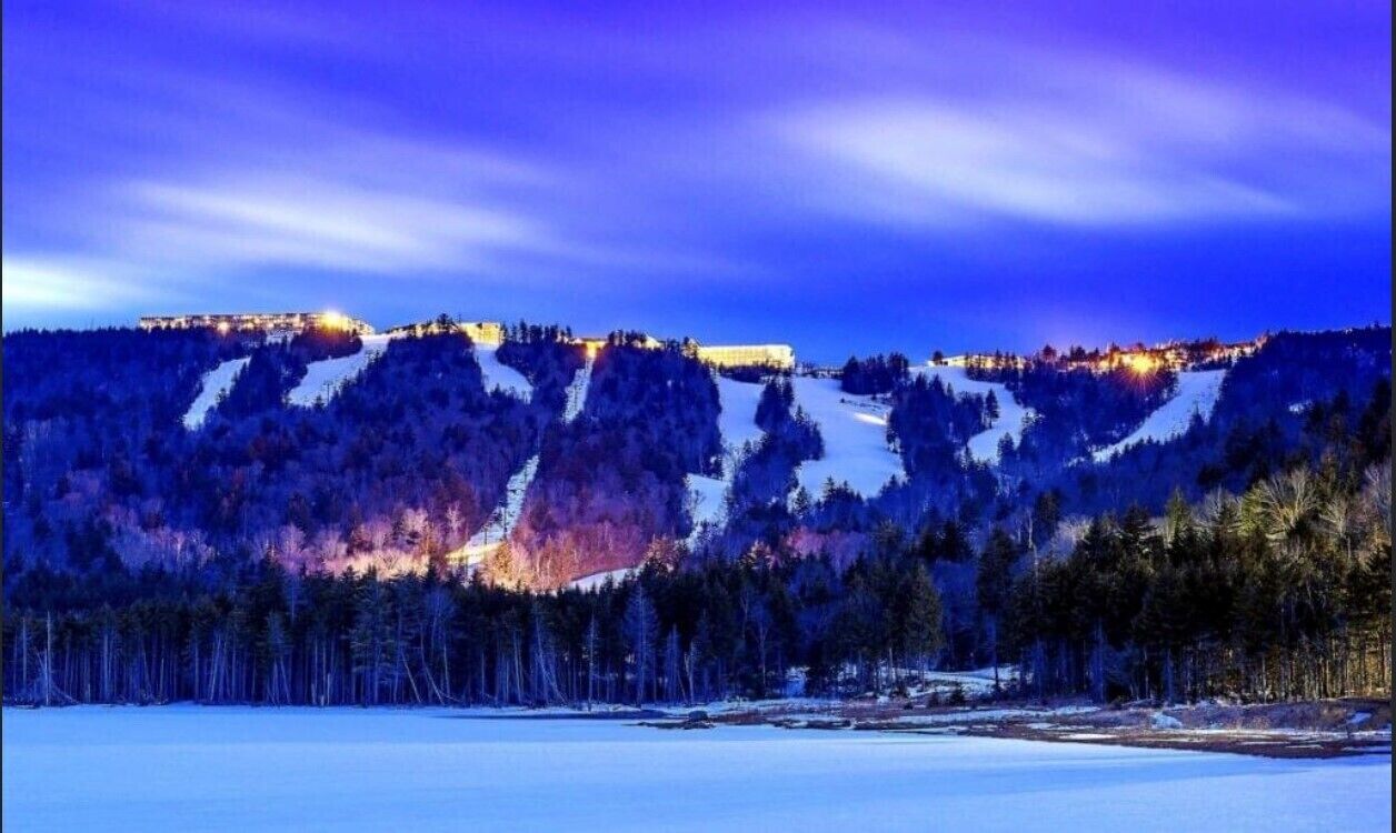 Un paisaje nevado con una cadena montañosa y un edificio iluminado al fondo.
