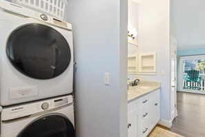 A laundry area with stacked washers and dryers, a bathroom with a sink and mirror, and a view of the outside balcony.