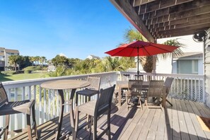 Eine Holzterrasse mit Gartenmöbeln, einem roten Sonnenschirm und Blick auf eine Wohngegend mit Häusern und Grünflächen.
