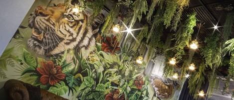 Un área de descanso con un mural de un tigre, plantas colgantes y mobiliario moderno.