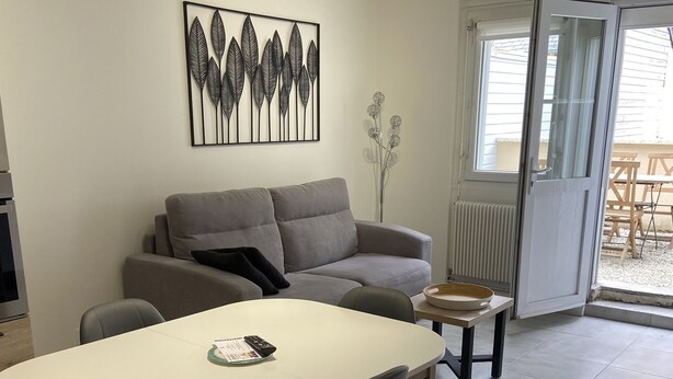 Ein modernes Wohnzimmer mit grauem Sofa, einem Esstisch mit Stühlen, einem Couchtisch und einem großen Fenster mit Blick nach draußen.