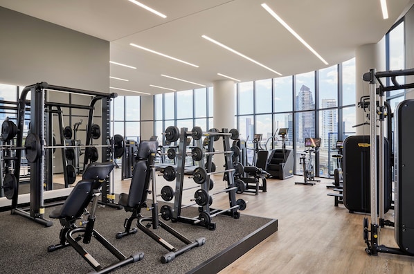 A modern gym with various weightlifting equipment, large windows, and a city view. - Oakwood Premier Melbourne (Melbourne)
