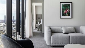 A modern living room with a grey sofa, a black chair, and a city view through large windows. - Oakwood Premier Melbourne (Melbourne)