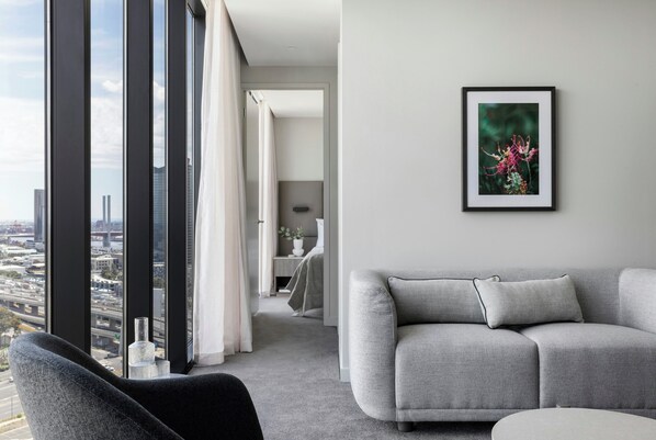 Een moderne woonkamer met een grijze bank, een zwarte fauteuil en een stadszicht door grote ramen.
