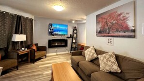Ein Wohnzimmer mit einer Couch, einem Couchtisch, einem Fernseher, einem Kamin und einem Bild an der Wand.