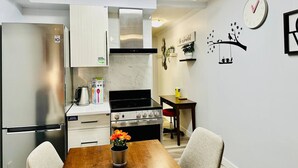 Et kompakt køkken med køleskab, komfur og mikrobølgeovn. Der er et spisebord med stole og en vase med blomster.