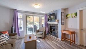 Ein Wohnzimmer mit Sofa, Sesseln, Couchtisch, Kamin und Fernseher.