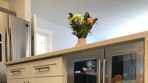 Eine Küche mit weißen Schränken, einem Edelstahlkühlschrank und einer Vase mit Blumen darauf.