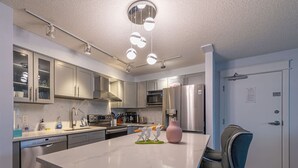 A modern kitchen with a central island, stainless steel appliances, and a seating area with a chair. - Mountain View/Full Kitchen/BBQ/AC/King Bed (Canmore)