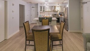 A modern kitchen with white cabinets, stainless steel appliances, and a dining area with wicker chairs. - Mountain View/Full Kitchen/BBQ/AC/King Bed (Canmore)