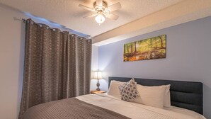 A bedroom with a bed, a headboard, a painting, a nightstand, and a ceiling fan. - Mountain View/Full Kitchen/BBQ/AC/King Bed (Canmore)